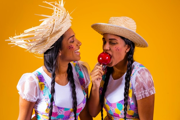 Beautiful twin girls in june party clothes eating a toffee apple