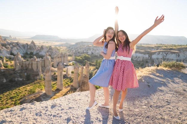 A beautiful two girl in a retro dress at sunrise is happy posing against the background of the mountain landscape in Cappadocia