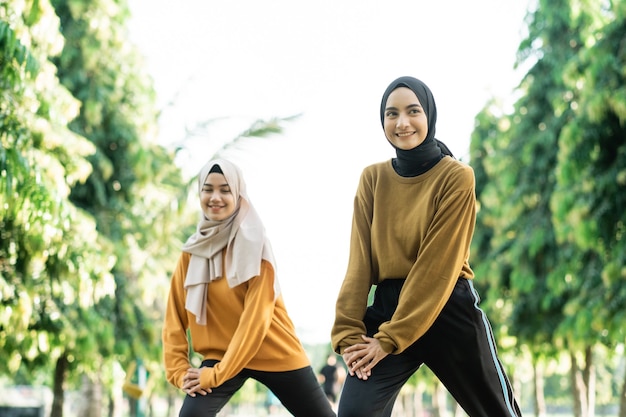 Beautiful two Muslim girls in headscarves do lunges movement before outdoor sports in the park