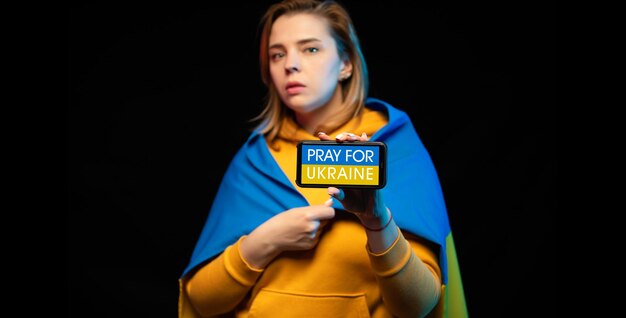 国家旗とスマートフォンを手にした美しいウクライナの少女と電話でPRAYFORUKRAINE反戦支援の実際の概念ロシア・ウクライナ戦争STOP WAR