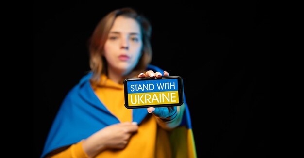 国家旗とスマートフォンを手に持った美しいウクライナの少女が電話をかけて立つSTANDWITHUKRAINE反戦支援の実際の概念ロシア・ウクライナ戦争ウクライナのための祈りSTOP WAR