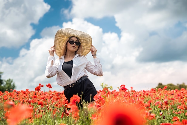 Bella signora ucraina da sola in cappello di paglia al campo di fiori di papaveri, sexy, giornata di sole