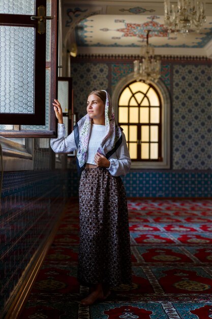 A beautiful Ukrainian woman in a scarf on her head stands in the mosque by the window and prays for peace