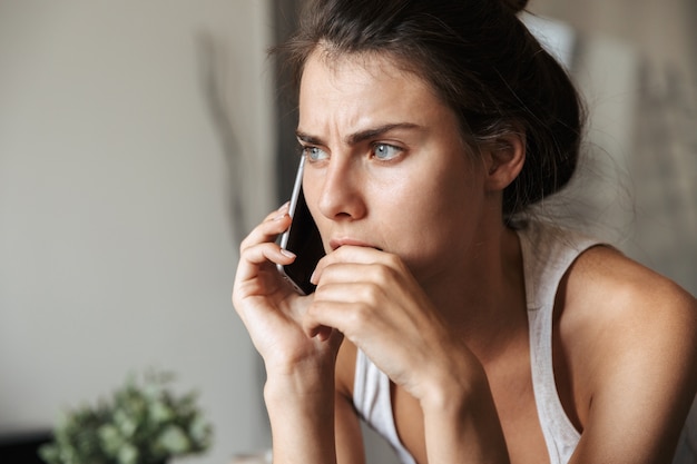 Bella giovane donna sconvolta posa su un divano a casa, utilizzando il telefono cellulare