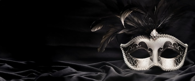 Beautiful venetian carnival mask with feather on dark fabric background in panoramic size