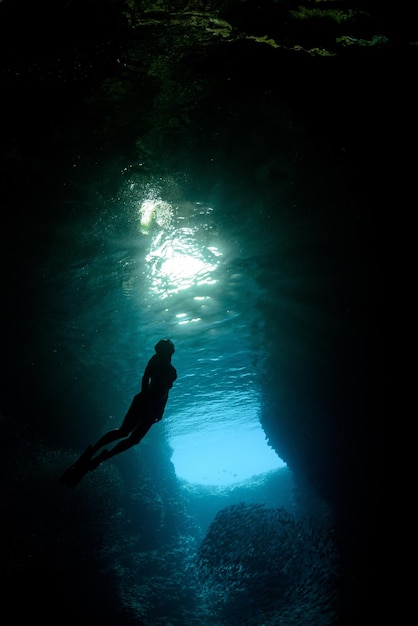 Beautiful vertical shot of a diver silhouette swimming through blue water