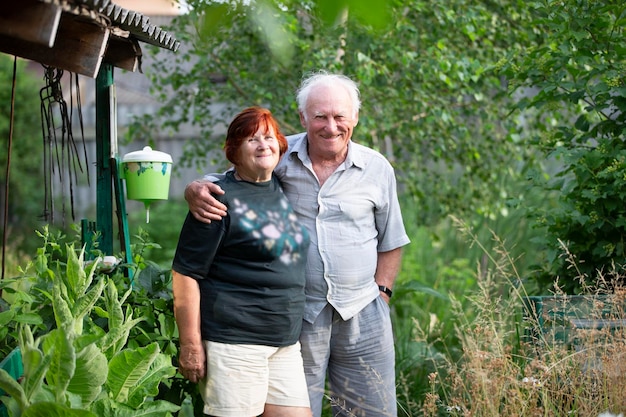 A beautiful very elderly couple hugs and looks at the camera at the dacha