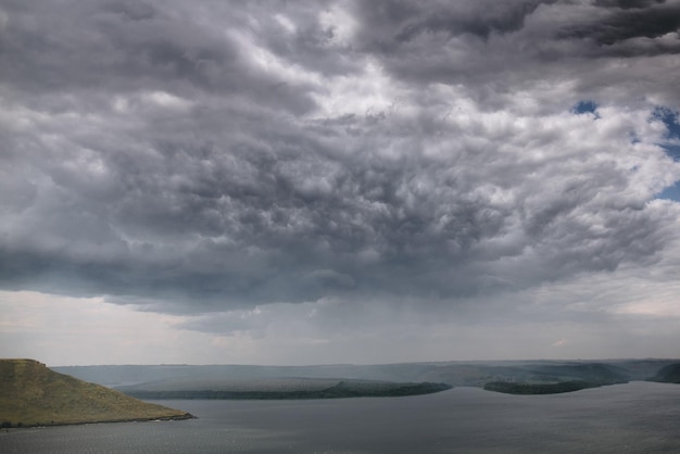 Beautiful view on big lake among hills and rain from clouds\
river and cliffs landscape bakota lake and dnister river in ukraine\
travelling and exploring national park