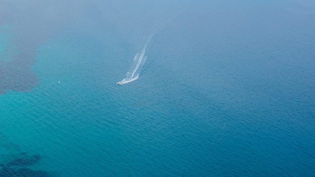 Beautiful view of the blue sea surface with passing small ship from the famous rock of Penon de Ifach, Spain. Natural background.