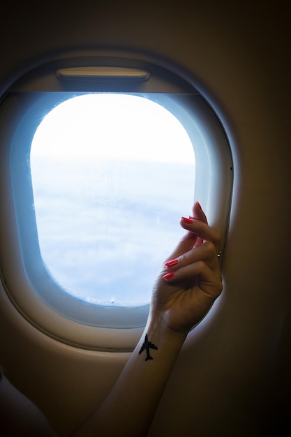 Beautiful view from the airplane window on the air clouds hand of a girl with a tattoo