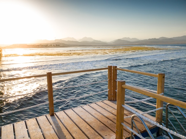 Beautiful view from the wooden pier or bridge on calm ocean sea waves and sunset over the mountains