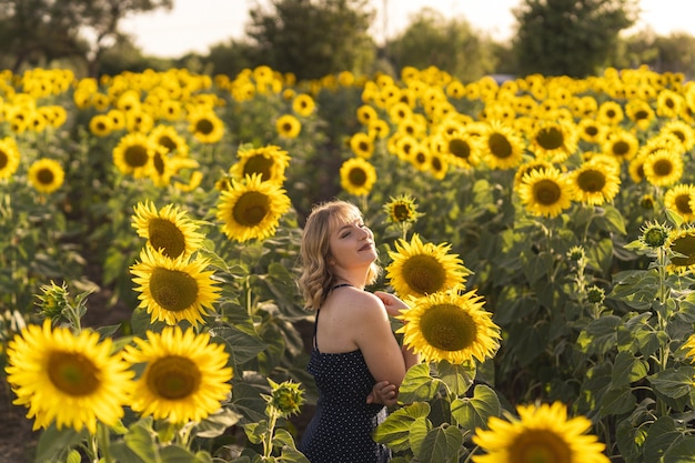 Beautiful view of a girl posing next to sunflowers growing in the field on a summer day