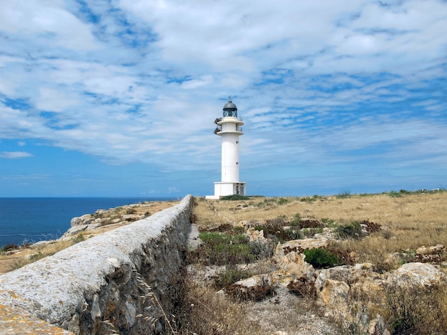 Beautiful view of the lighthouse on a cliff under a cloudy sky in Formentera, Spain