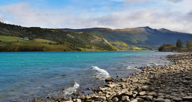 緑の丘と山々 とノルウェーの青い水と岩の多いビーチの美しい景色