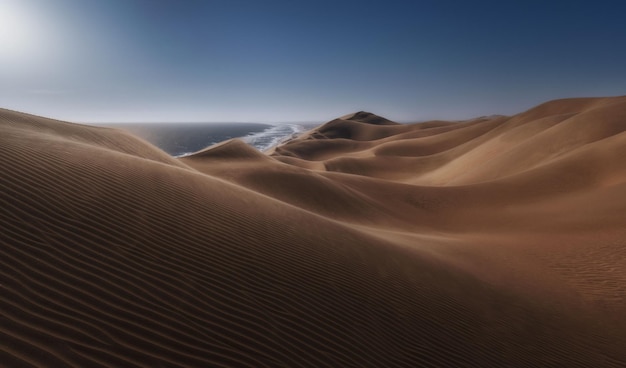 Beautiful view of soft dunes with sea in the background under clear sky