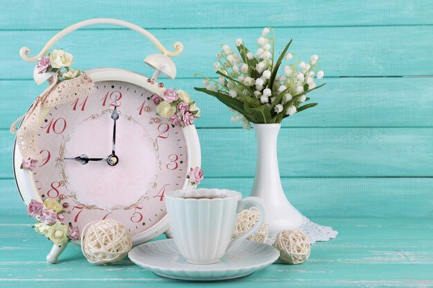 Beautiful vintage alarm clock with flowers and cup of tea on blue wooden background