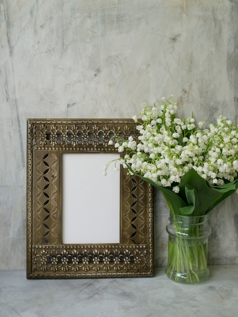 Photo beautiful vintage frame with  bouquet of lilies of the valley on a gray background.