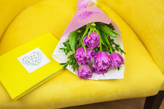 Beautiful violet bouquet of tulips on a yellow stool and yellow book