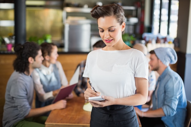 Beautiful waitress standing by customers in restaurant