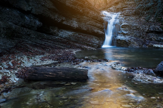 Beautiful waterfall at mountain river in colorful autumn forest with red and orange leaves at sunset. Nature landscape