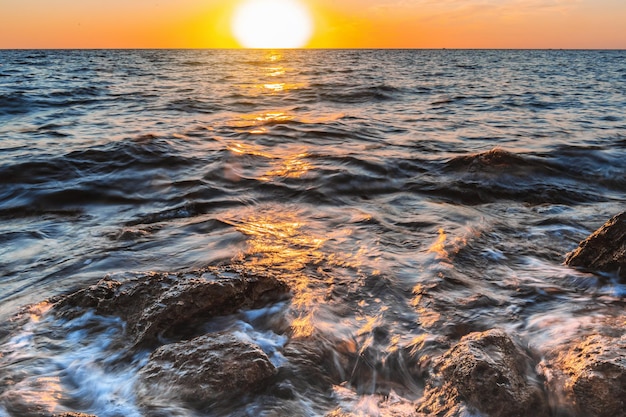 Beautiful waves on a long exposure beating against rocks against the background of a bright sunset