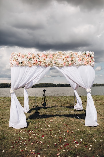 Beautiful wedding arch with flowers View over white wedding arch with flowers on the top and rose petals scattered on the grass  Situated by the river on cloudy day 