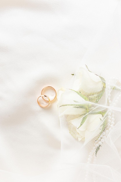 Красивый свадебный фон для дизайна Два обручальных кольца на атласной ткани с живыми белыми бутонами роз Вертикальное приглашение на открытку