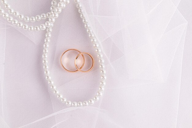 写真 2つの金の指輪と真珠のビーズのひもが付いた美しい結婚式の背景白い新婦のベールポストカードの招待状の表紙コピースペース