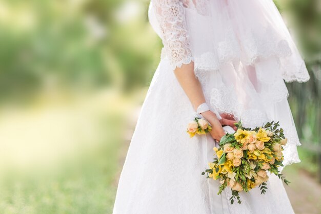 Beautiful wedding bouquet in the hands of the bride. behind the back. yellow, white flowers with ribbon