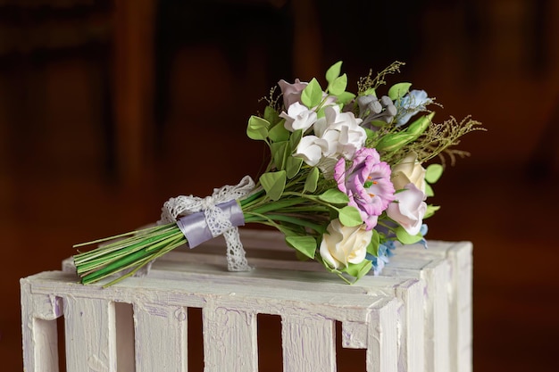 Beautiful wedding bouquet made of polymer clay white lies on wooden box tied with a handmade ribbon