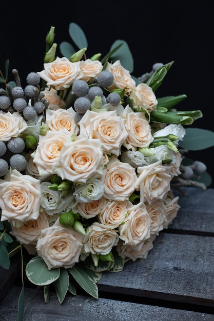 Красивый свадебный букет из кустистой кремовой розы, эвкалипта, брунея, питтоспорума и лизиантуса на черной стене.