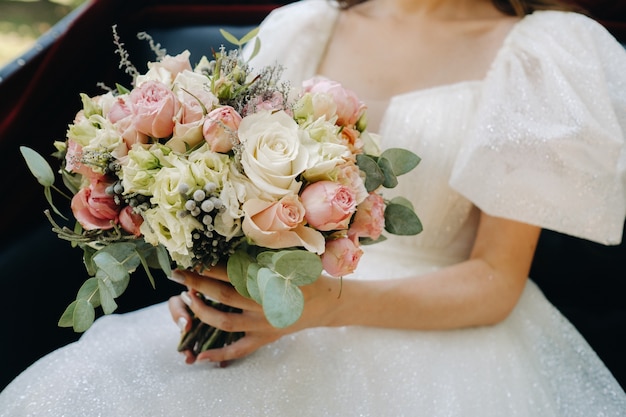 A beautiful wedding bouquet with roses in the hands of the bride