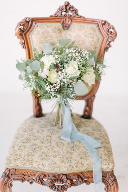 Beautiful wedding bouquet with white roses, pine and eucalyptus lying on the vintage chair