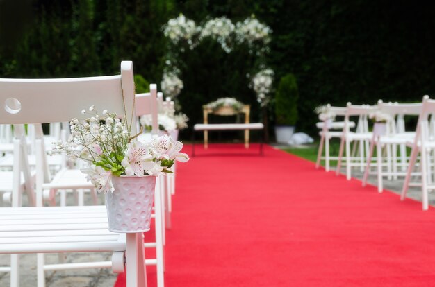 Beautiful Wedding ceremony decoration, rustic altar decorated with lilies, alstroemerias and chrysanths flowers behind  ivy wall, red carpet with whites chairs. Wedding day concept. Space for text.