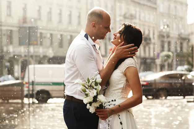 美しい結婚式のカップルは雨の中で街を歩いて幸せそうに見える