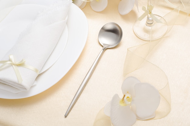 Beautiful wedding festive table setting with white napkin, white dishes and white orchid on a light silk tablecloth