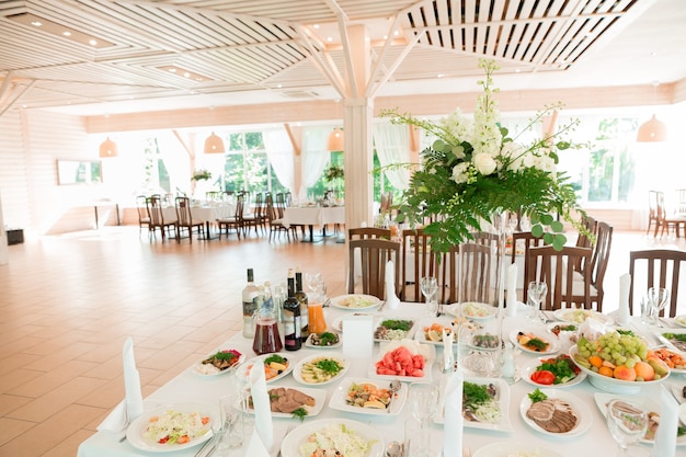 Beautiful wedding floral decoration on a table with catering food in a light restaurant hall with white tablecloths