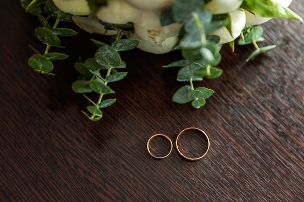 Beautiful wedding rings lie on wooden surface against background of bouquet of flowers.