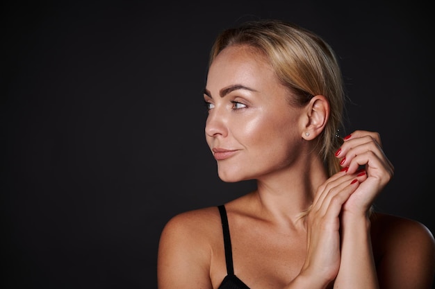 Beautiful wellgroomed young Caucasian woman with blond hair clean radiant healthy tanned skin and wellgroomed manicure looks aside posing on a black background with copy ad space for ads