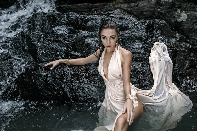 A beautiful wet girl in  a fashion long dress on a waterfall 