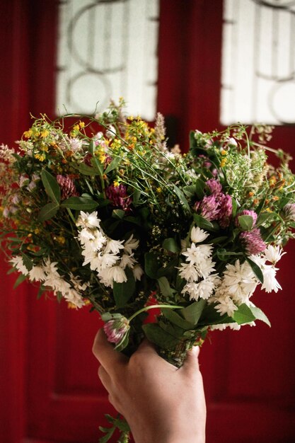 Beautiful white flowers bouquet in hand at rustic wooden red door simple adorning