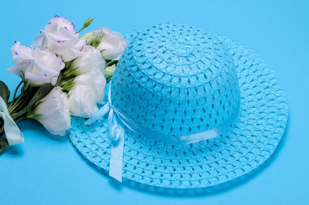 Beautiful white flowers eustoma and female blue hat on a bright blue background