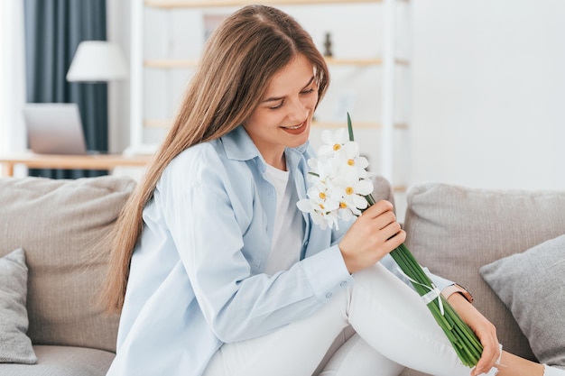 Beautiful white flowers in hands Young beautiful woman is home alone in domestic room