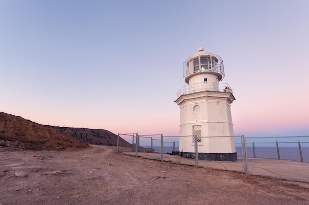 Beautiful white lighthouse on the ocean coastline at sunset Landscape