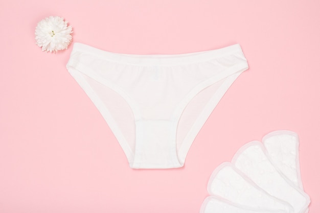 Beautiful white panties with sanitary napkins on pink background. Women underwear set. Top view.