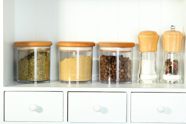 Photo beautiful white shelves with spices in glass bottles