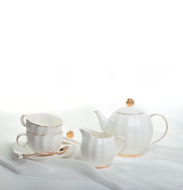 Beautiful white still life with white dishes for tea, coffee, on a white background with silk draper