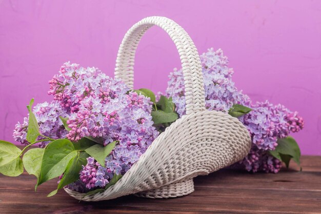 Beautiful white vintage wicker basket on a wooden table Lilac flowers in a retro basket