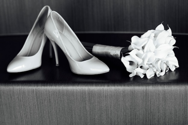 Фото Красивый белый свадебный букет из лилий лежит рядом с обувью невесты