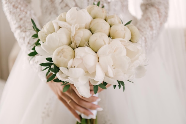 Beautiful white wedding bouquet of peonies in the hands of the bride